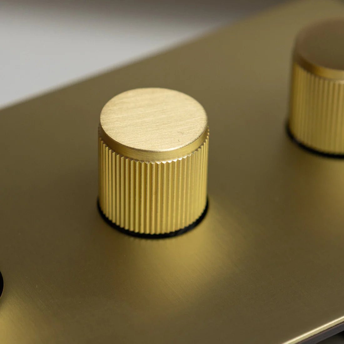 Brass bee Satin Brass Switches and Sockets in straight knurled design featuring textured knobs, with a smooth metallic finish and contrasting black accents.
