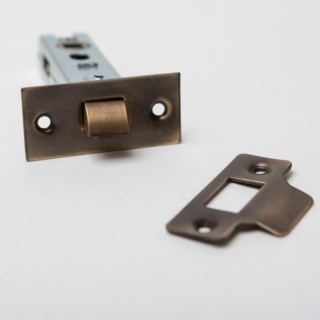 Brass bee Designer Levers Bolt Through Tubular Latch with a 76mm case, featuring a brass finish and a rectangular strike plate, viewed from an angle to show the latch mechanism and plate.