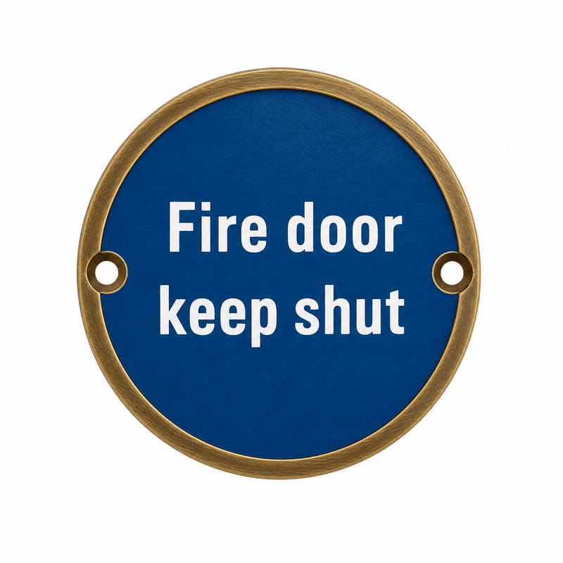 Zoo Hardware Fire Door Keep Shut Sign in round shape with a blue background and white lettering, featuring two holes for mounting.