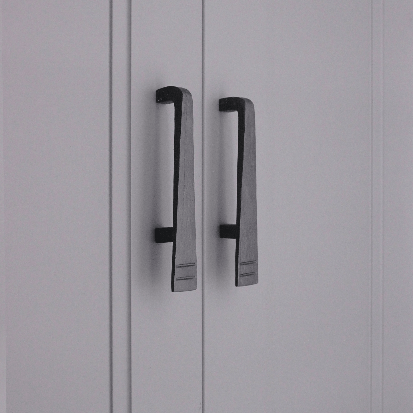 Spira Brass Skeg Pull Handle in a dark finish, featuring a sleek design with horizontal grooves, mounted on cabinet doors.