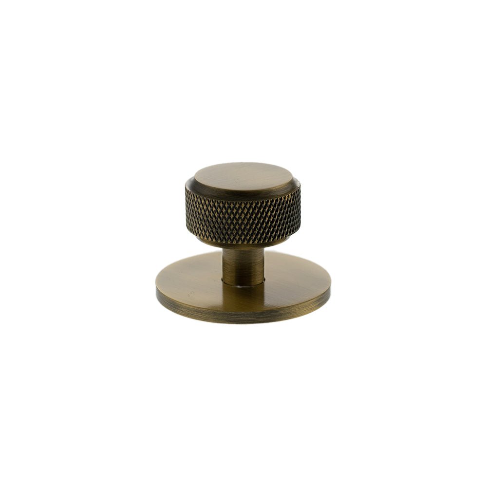 Atlantic Millhouse Brass Eiffel Knurled Round Cabinet Knob Handle on Backplate features a textured knurled design in an antique brass finish, mounted on a circular backing plate for easy attachment.