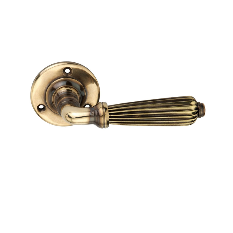 Spira Brass Regency Door Handle in a classic design featuring a ribbed handle and a round backplate, all in an aged brass finish. The handle showcases detailed grooves and a smooth grip.