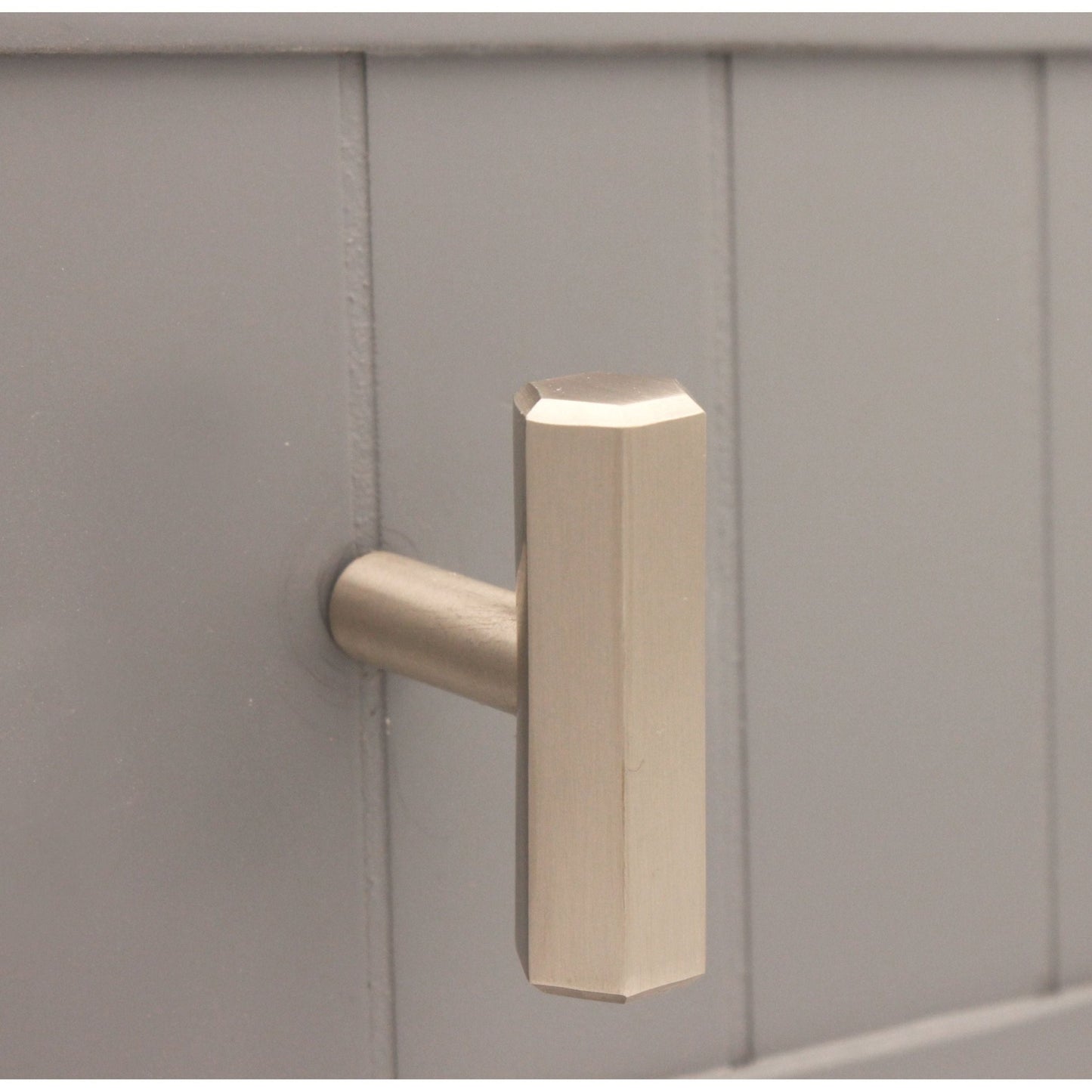 Spira Brass Hexagonal T bar Cupboard Pull in a brushed brass finish, featuring an octagonal design and a sturdy, simple handle. It is mounted on a grey cabinet surface.