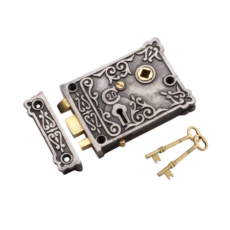 Spira Brass Floral Rim Lock in antique silver finish, featuring an intricate floral design, with two brass keys included. The lock is shown with the strike plate and has visible keyhole and bolt mechanism.