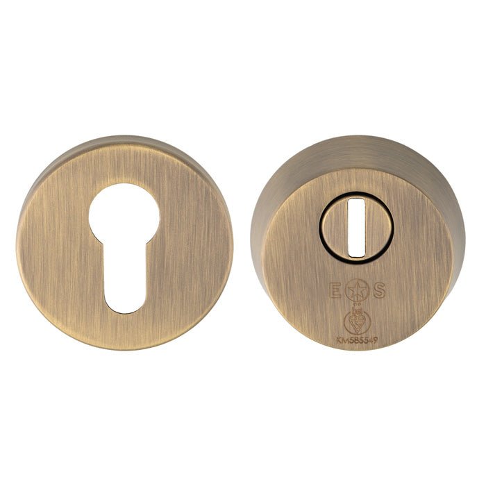 Carlisle Brass 2 Star Security Escutcheon in an antique brass finish, featuring a keyhole cutout and a separate circular part with a secure slot design. Both components are made of sturdy metal for durability.