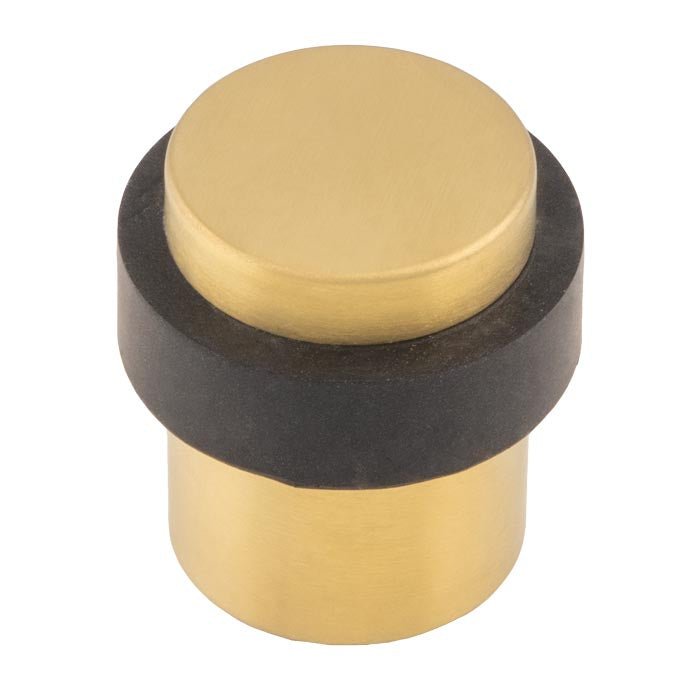 Carlisle Brass Floor Mounted Pedestal Door Stop in brass finish with a cylindrical body and a black rubber ring, designed to securely hold doors open while preventing damage to walls and doors.