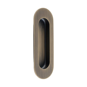 Carlisle Brass Radius Flush Pulls in an antique brass finish, featuring a sleek oval design with a brushed texture, designed for easy gripping and installation on doors or cabinets.