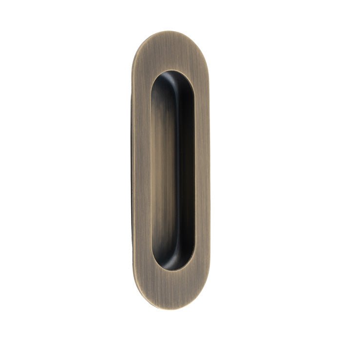 Carlisle Brass Radius Flush Pulls in an antique brass finish, featuring a sleek oval design with a brushed texture, designed for easy gripping and installation on doors or cabinets.