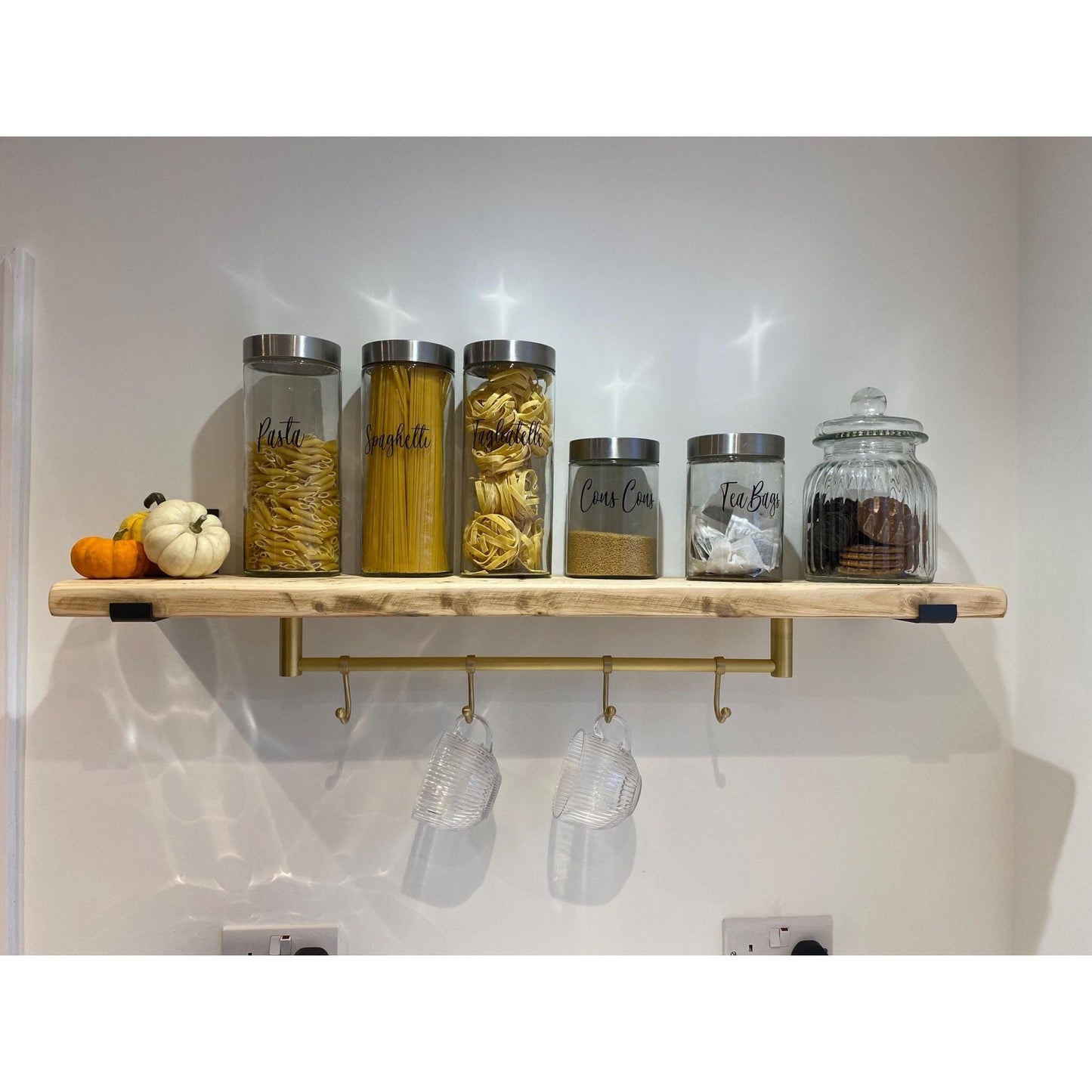Brass bee Satin Brass Hook Rail with 3 Brass Hooks, made of solid brass, mounted below a wooden shelf displaying storage jars. The rail features three hooks for hanging items, enhancing organization.