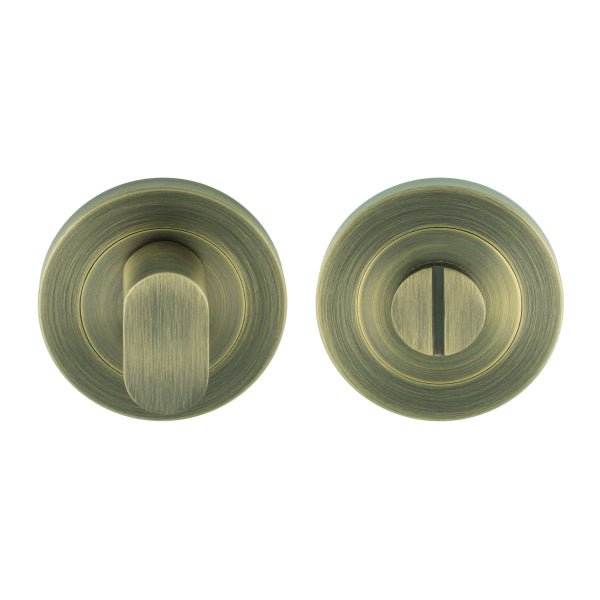 Carlisle Brass SWL Thumbturn in antique brass finish, featuring a cylindrical lever and a matching round base plate. The design includes a slot for key access alongside the thumbturn mechanism.