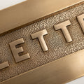 Brass bee Letterplate in a brushed brass finish featuring raised letters on a textured background. The design includes a rectangular shape with a polished border, suitable for mounting on doors or walls.