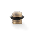 Alexander & Wilks Dome Top Floor Mounted Door Stop with a brushed brass finish and a black rubber ring at the base, designed to prevent doors from damaging walls.