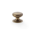 Alexander & Wilks Waltz Round Cupboard Knob on Stepped Rose in a brushed antique brass finish, featuring a smooth rounded top and a stepped base for grip.
