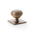 Alexander & Wilks Quantock Cupboard Knob on Square Backplate in antique brass finish, featuring a rounded knob atop a square base with a smooth texture.