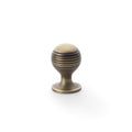 Alexander & Wilks Caesar Cupboard Knob on Round Rose features a ribbed design in an antique brass finish. The knob has a rounded top and a circular base, providing a classic look suitable for various cabinetry.