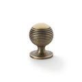 Alexander & Wilks Caesar Cupboard Knob on Round Rose in an antique brass finish, featuring a spherical shape with textured horizontal grooves and a flat top, designed for cabinet doors or drawers.