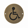 A round brushed brass accessibility symbol sign with two mounting holes, shown on a solid white background.