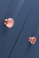 Carlisle Brass Oxford Knob in rose gold finish, featuring a smooth round shape suitable for cabinetry or furniture. The knob is clearly displayed against a blue panel background.