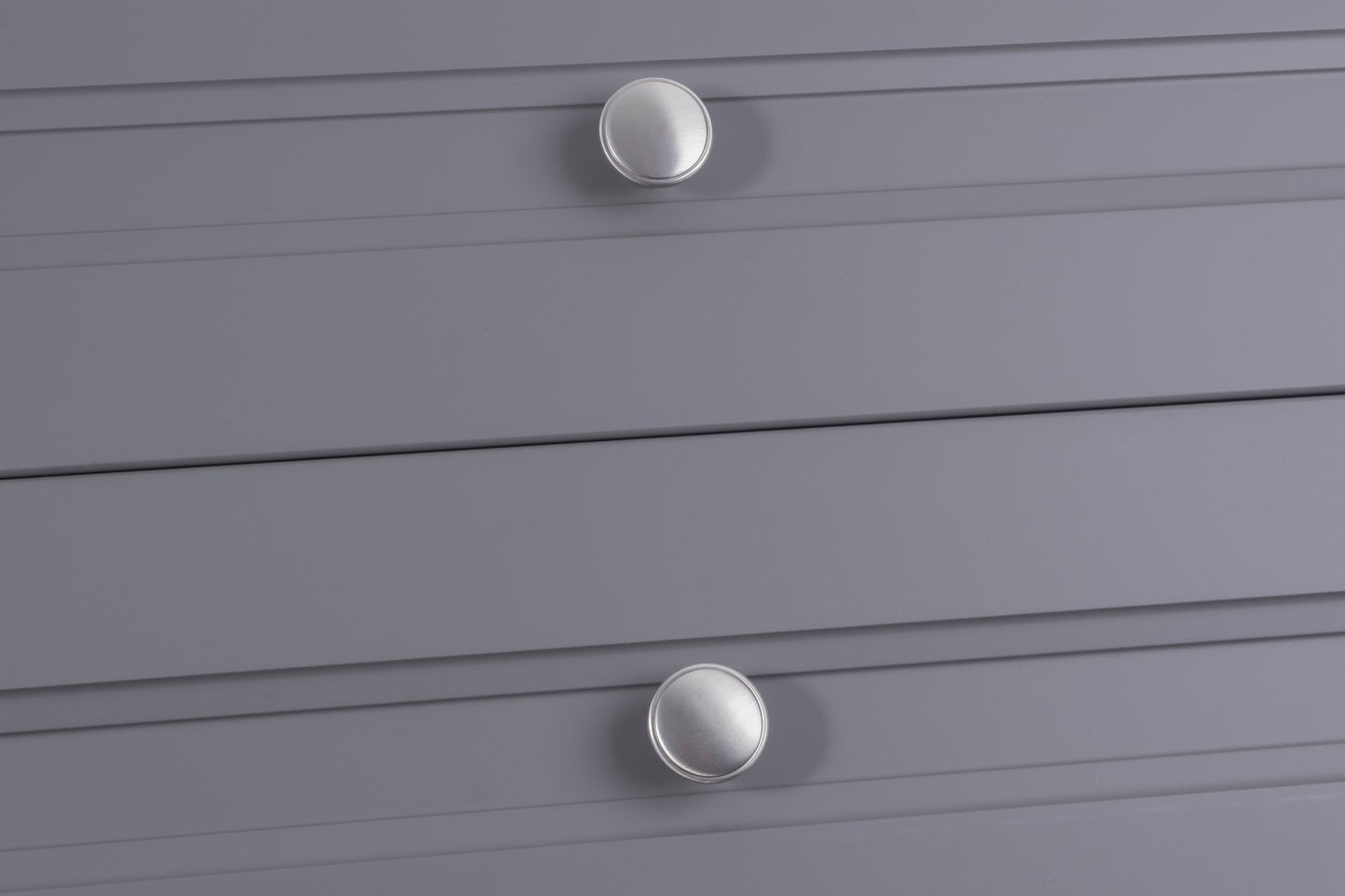 Carlisle Brass Oxford Knob in a brushed nickel finish, featuring a round, flat design installed on gray drawer fronts. The knob is positioned on horizontal lines of the drawers.