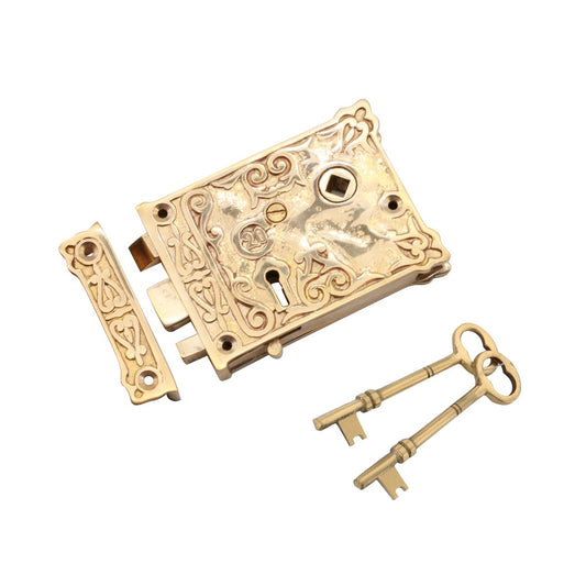 Spira Brass Floral Rim Lock in brass finish, featuring ornate detailing, a keyhole, and accompanied by two traditional keys. The lock includes a matching strike plate for installation.