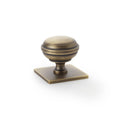 Alexander & Wilks Quantock Cupboard Knob on Square Backplate in antique brass finish, featuring a rounded knob design atop a square backplate.