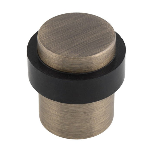Carlisle Brass Floor Mounted Pedestal Door Stop featuring a round, brushed bronze top and a black rubber base, designed to hold doors open securely.