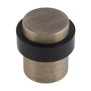 Carlisle Brass Floor Mounted Pedestal Door Stop featuring a round, brushed bronze top and a black rubber base, designed to hold doors open securely.